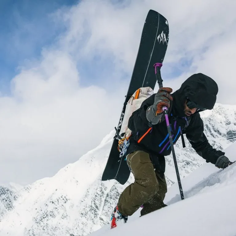 Splitboarder bootpacking up a steep snow slope with board on pack