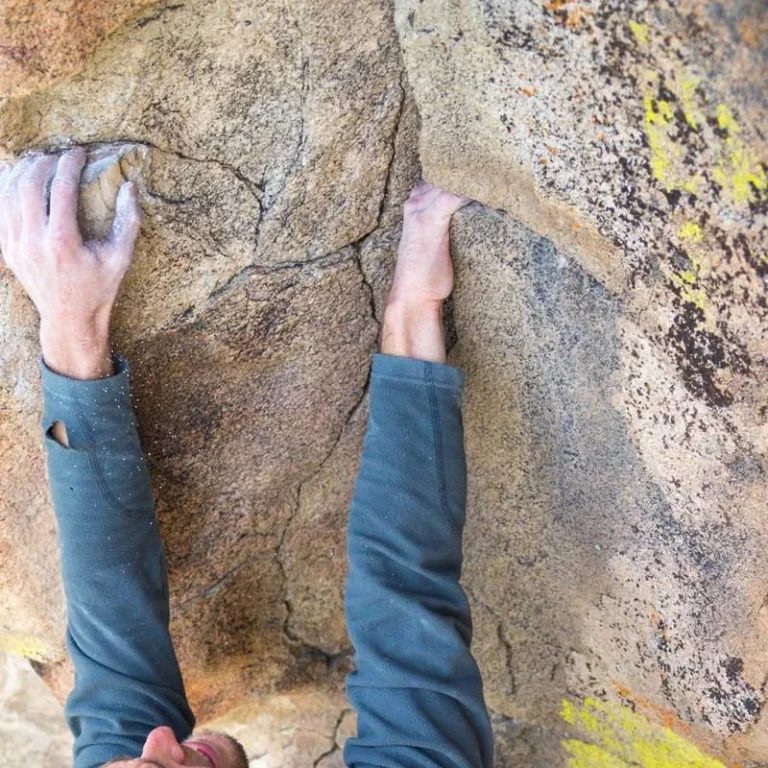 Chalked hands gripping a small crimp on granite